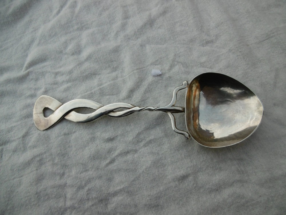 An Arts and Crafts sterling silver spoon with a twisted Celtic knot handle and a planished heart-shaped bowl.
