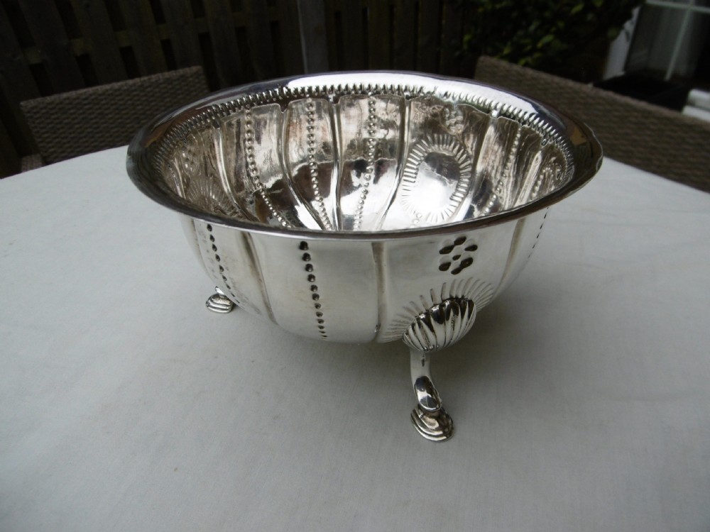 An antique George II sterling silver footed bowl featuring fluted sides, bead details, and shell-motif legs.