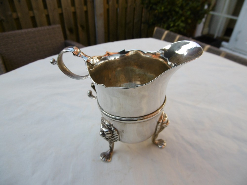 An 18th-century Georgian Irish silver helmet-shaped cream jug with a scalloped rim, scroll handle, and three lion mask feet.