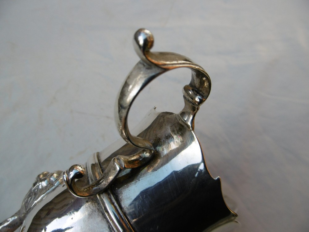 An 18th-century Georgian Irish silver helmet-shaped cream jug with a scalloped rim, scroll handle, and three lion mask feet. View IV