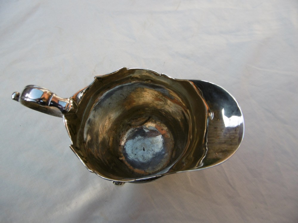 An 18th-century Georgian Irish silver helmet-shaped cream jug with a scalloped rim, scroll handle, and three lion mask feet. View V