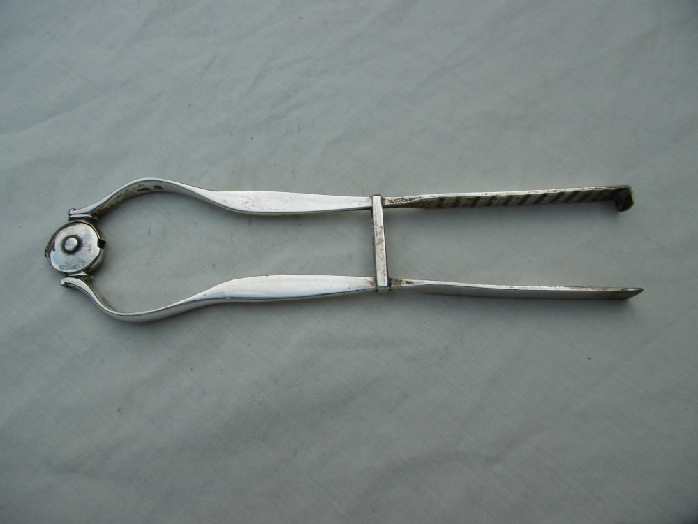 A pair of 1799 George III sterling silver serving tongs featuring a circular central boss with an engraved crest, curved arms, and a sliding restraint bar. View II
