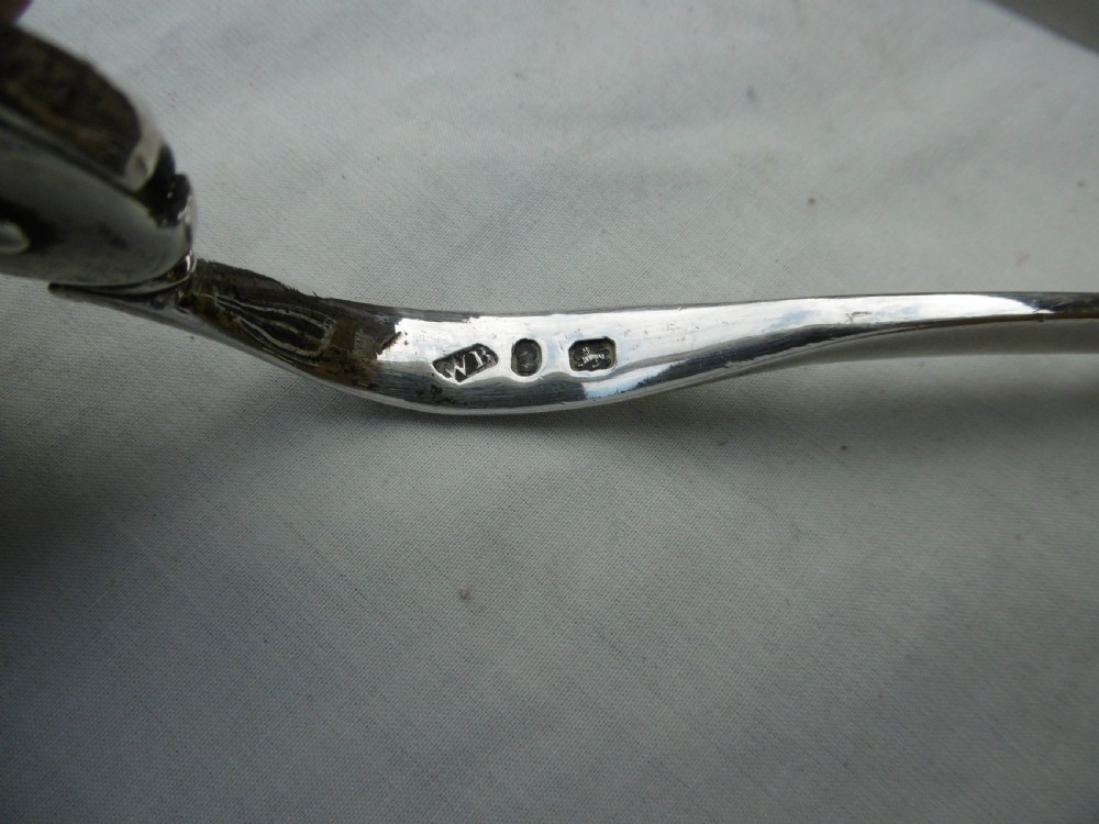 A pair of 1799 George III sterling silver serving tongs featuring a circular central boss with an engraved crest, curved arms, and a sliding restraint bar. View III