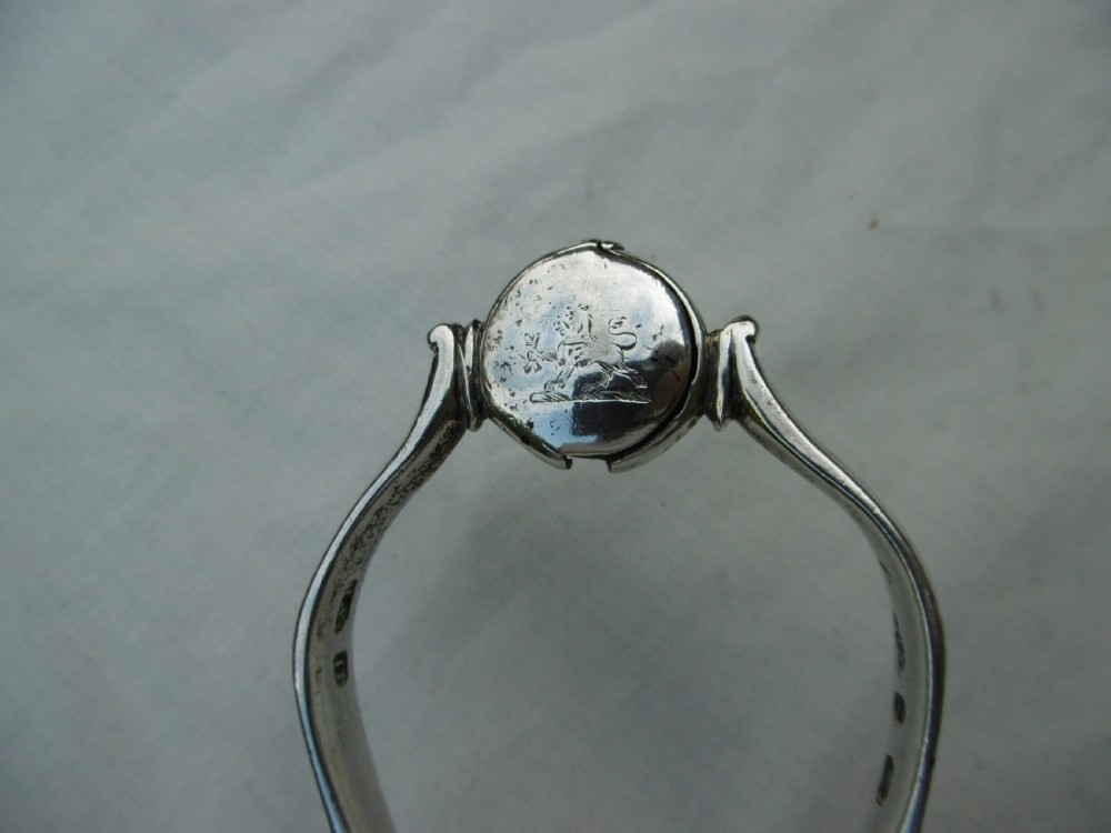 A pair of 1799 George III sterling silver serving tongs featuring a circular central boss with an engraved crest, curved arms, and a sliding restraint bar. View V