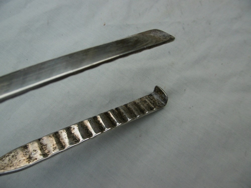 A pair of 1799 George III sterling silver serving tongs featuring a circular central boss with an engraved crest, curved arms, and a sliding restraint bar. View VI