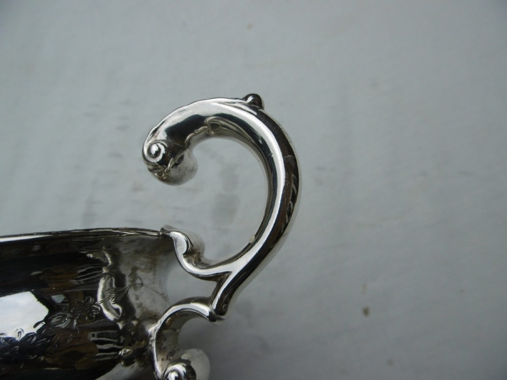 A 1778 Georgian sterling silver sauce boat featuring a beaded rim, a scroll handle, and a oval pedestal foot. View III
