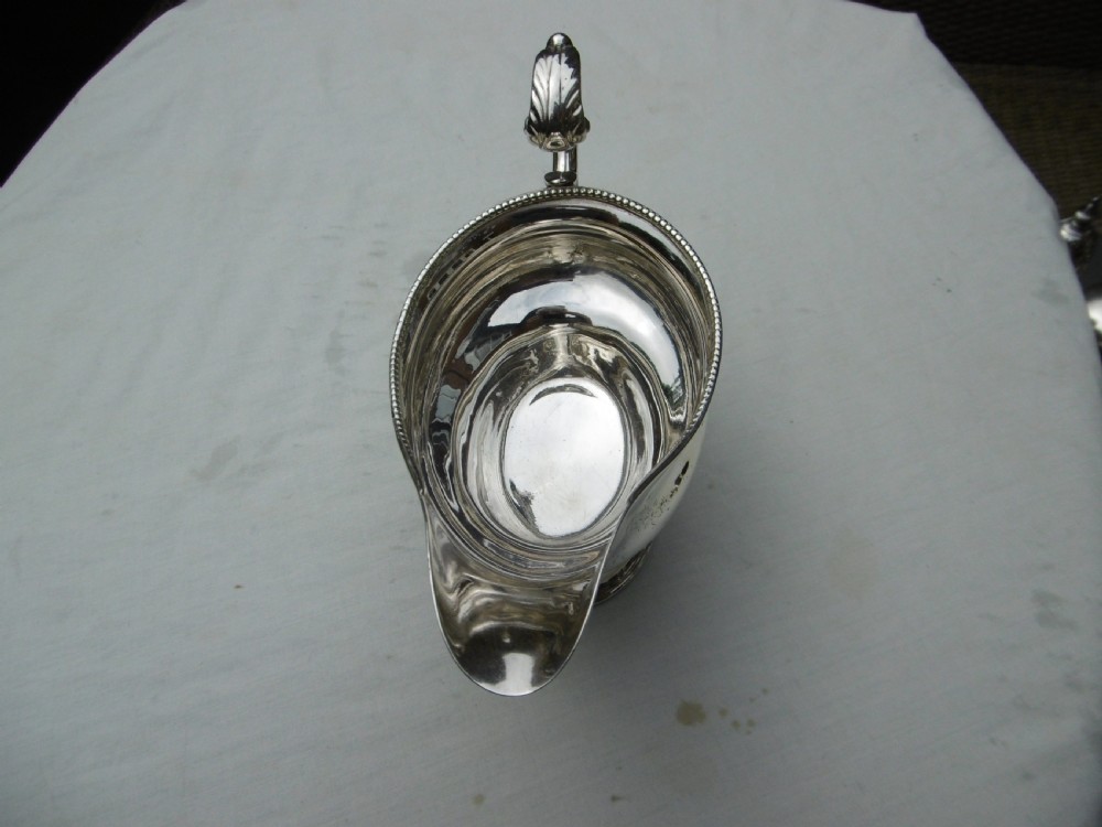 A 1778 Georgian sterling silver sauce boat featuring a beaded rim, a scroll handle, and a oval pedestal foot. View IV