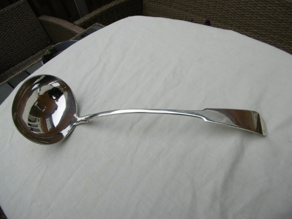 A Georgian Scottish provincial sterling silver soup ladle with a polished circular bowl and a long curved flat handle against a plain background.