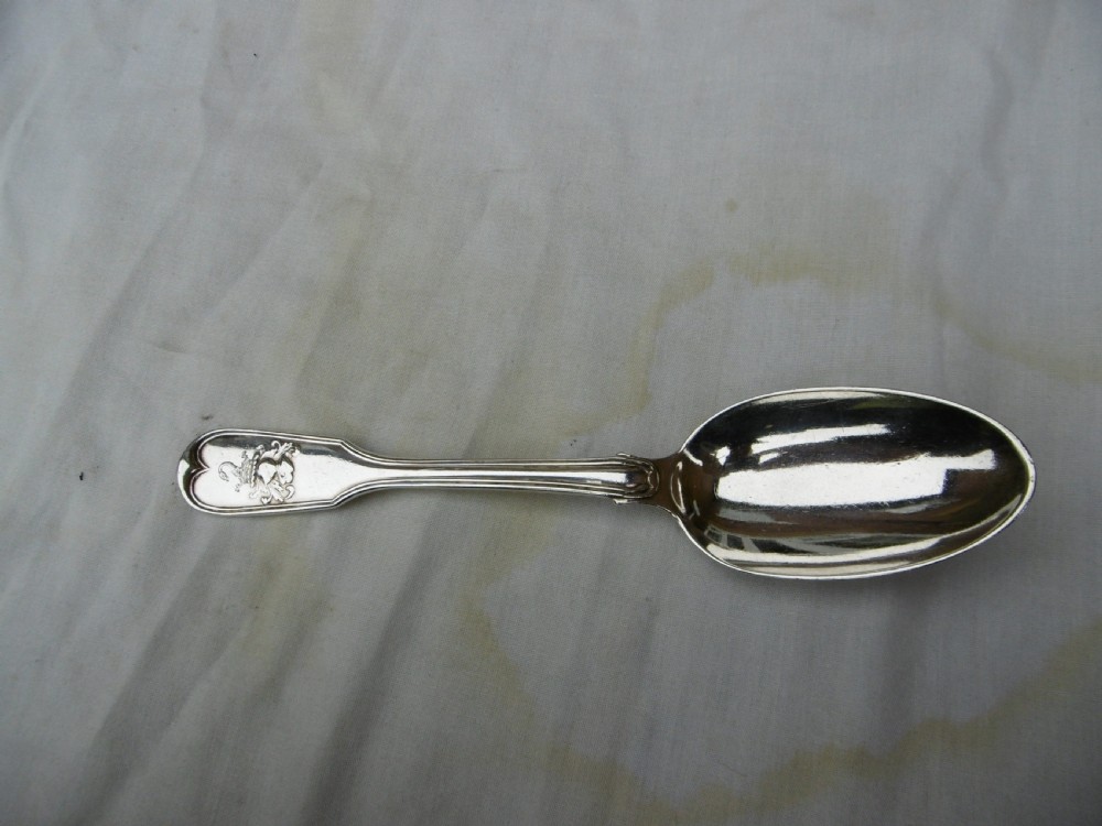 A Georgian sterling silver tablespoon featuring an engraved heraldic crest on the stem handle and an oval polished bowl.