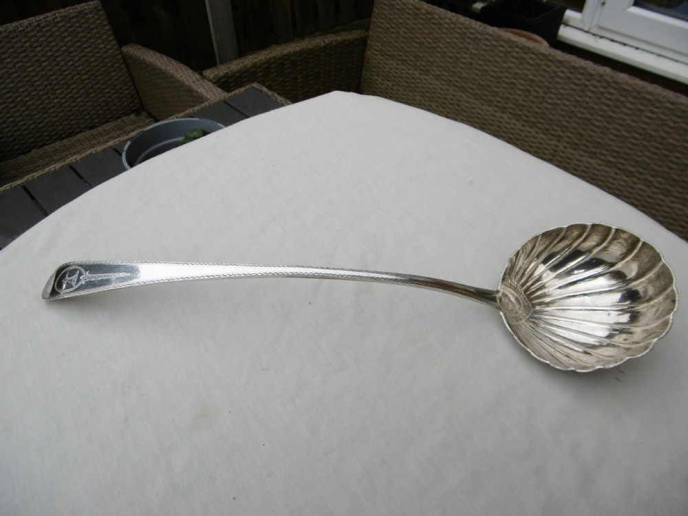 An 18th-century Georgian sterling silver soup ladle with an engraved crest on the handle and a fluted shell bowl.