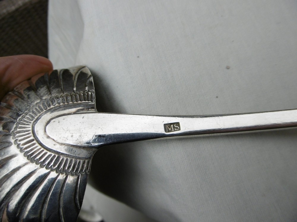 An 18th-century Georgian sterling silver soup ladle with an engraved crest on the handle and a fluted shell bowl. View V