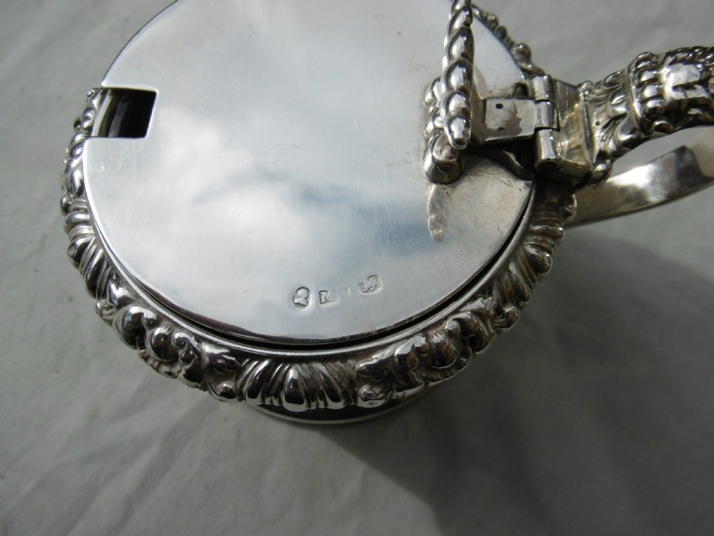 A circular Georgian sterling silver mustard pot featuring a hinged lid with a leaf motif finial and gadrooned border. View III