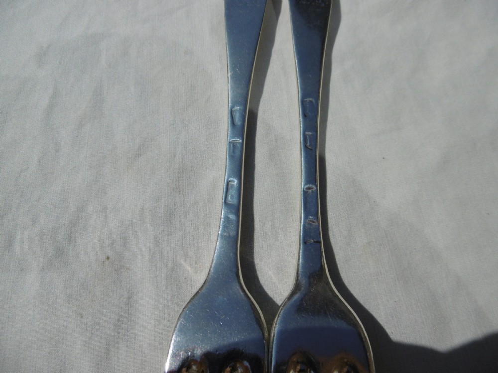A pair of early 18th-century George I Britannia standard silver three-pronged forks displayed on a white fabric surface. View III