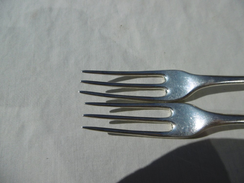 A pair of early 18th-century George I Britannia standard silver three-pronged forks displayed on a white fabric surface. View V