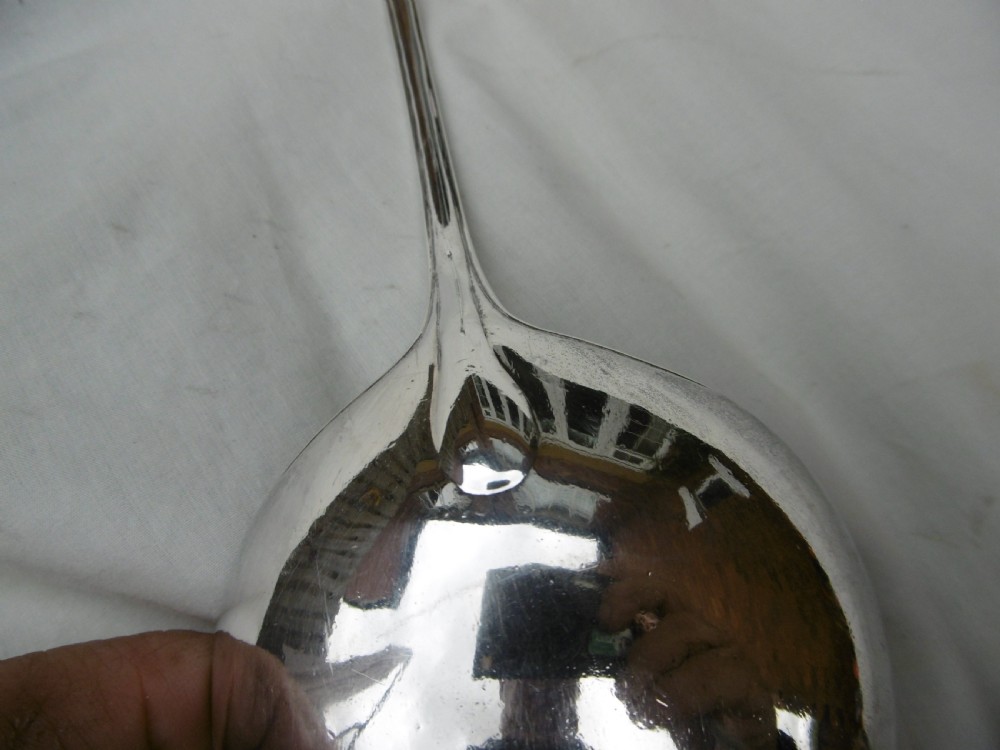 A Georgian sterling silver soup ladle featuring a long curved stem, a circular bowl, and official assay hallmarks near the terminal. View IV