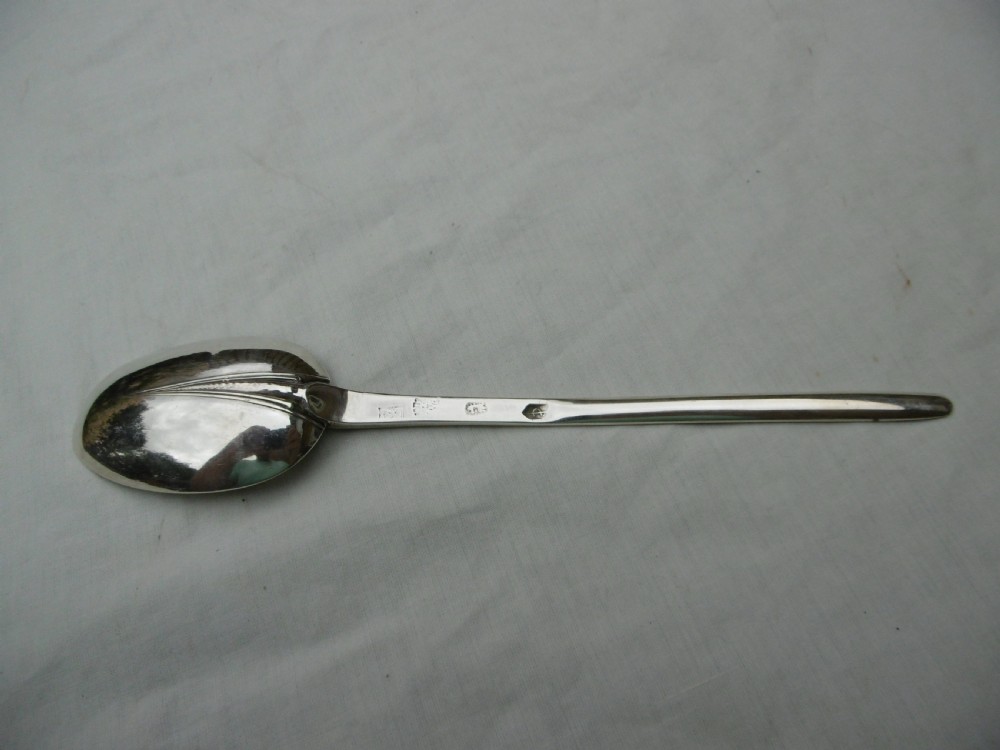 An antique Queen Anne silver marrow spoon showing an oval bowl with a rat-tail joint and a narrow scoop stem stamped with hallmarks.