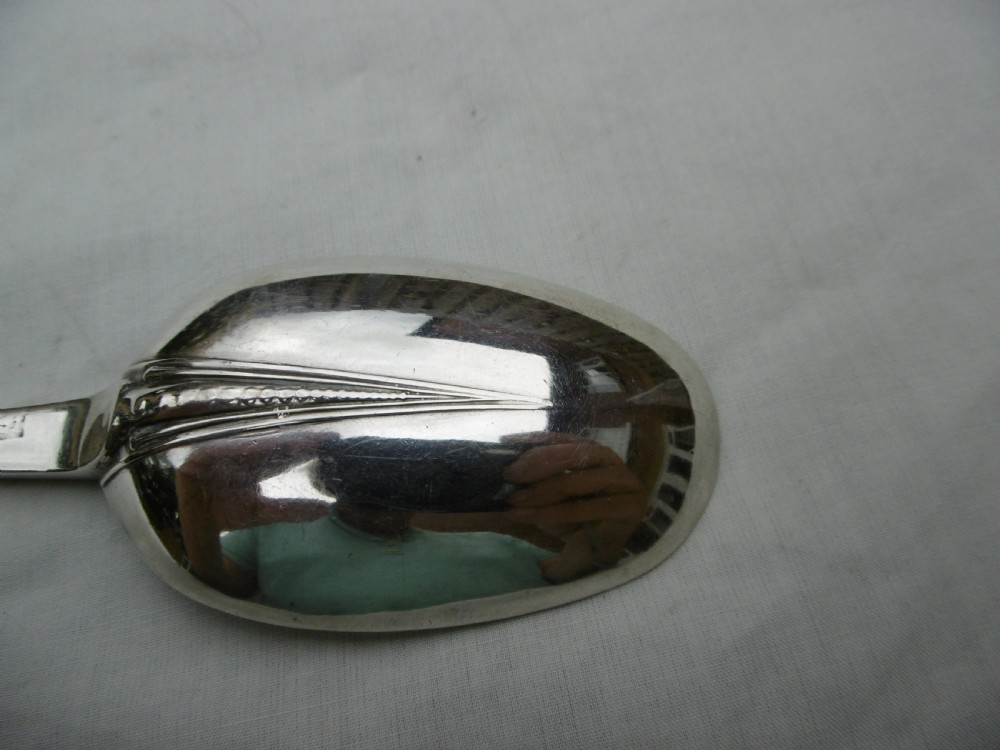 An antique Queen Anne silver marrow spoon showing an oval bowl with a rat-tail joint and a narrow scoop stem stamped with hallmarks. View IV