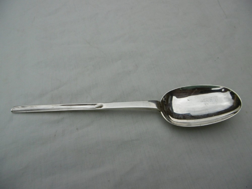 An antique Queen Anne silver marrow spoon showing an oval bowl with a rat-tail joint and a narrow scoop stem stamped with hallmarks. View V