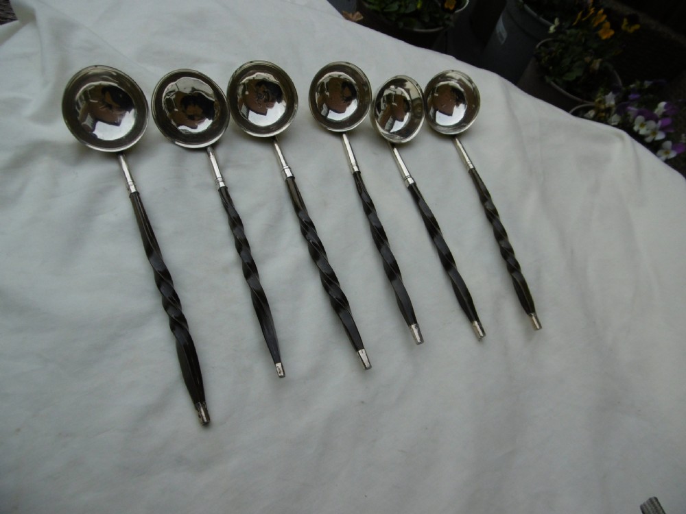 A set of six Georgian silver toddy ladles with circular bowls and dark twisted handles laid in a row.