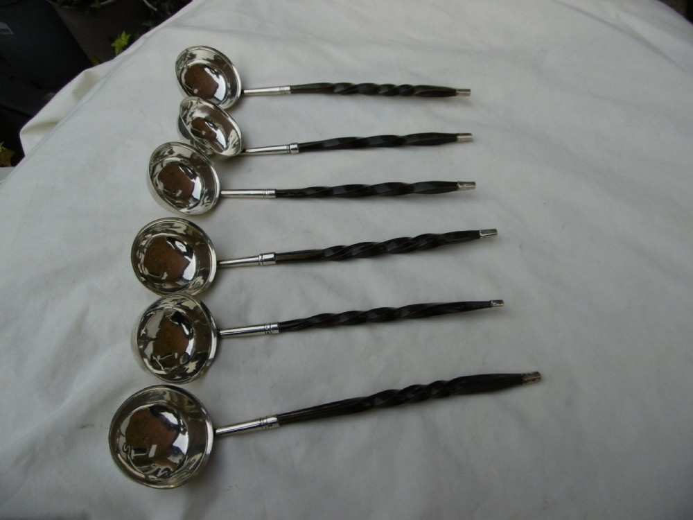 A set of six Georgian silver toddy ladles with circular bowls and dark twisted handles laid in a row. View II