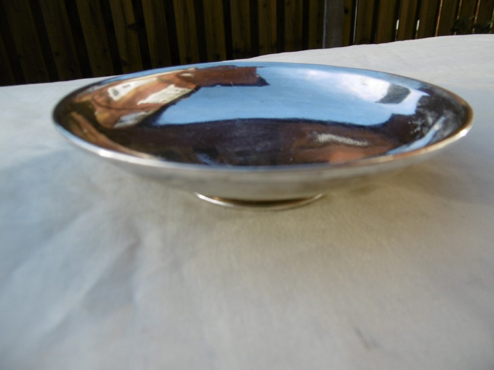 A circular Georgian sterling silver paten dish with a moulded rim resting on a short foot ring.