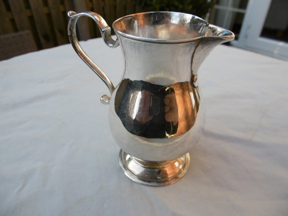 A George II sterling silver cream jug featuring a baluster body, sparrow beak spout, loop handle, and circular pedestal foot.