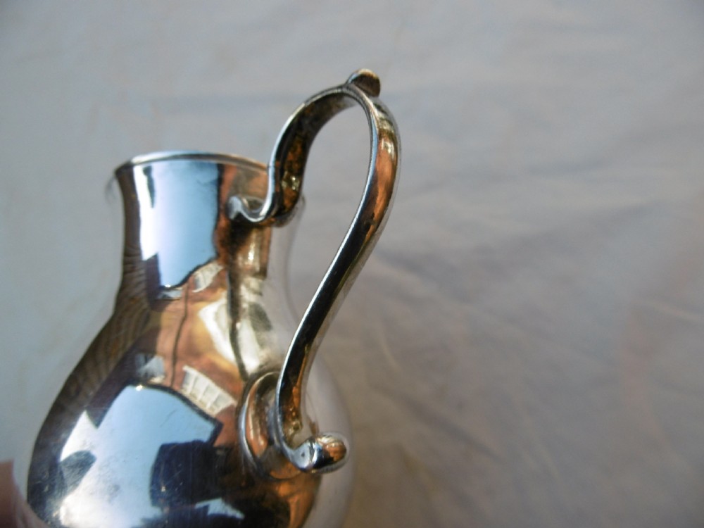A George II sterling silver cream jug featuring a baluster body, sparrow beak spout, loop handle, and circular pedestal foot. View IV