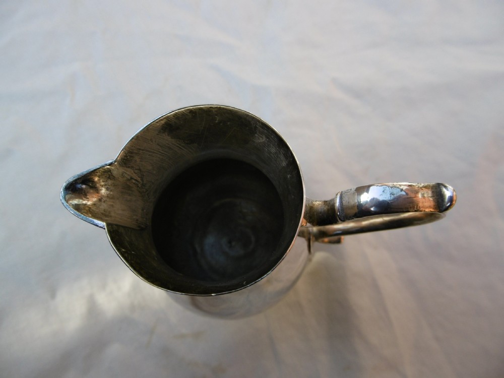 A George II sterling silver cream jug featuring a baluster body, sparrow beak spout, loop handle, and circular pedestal foot. View V