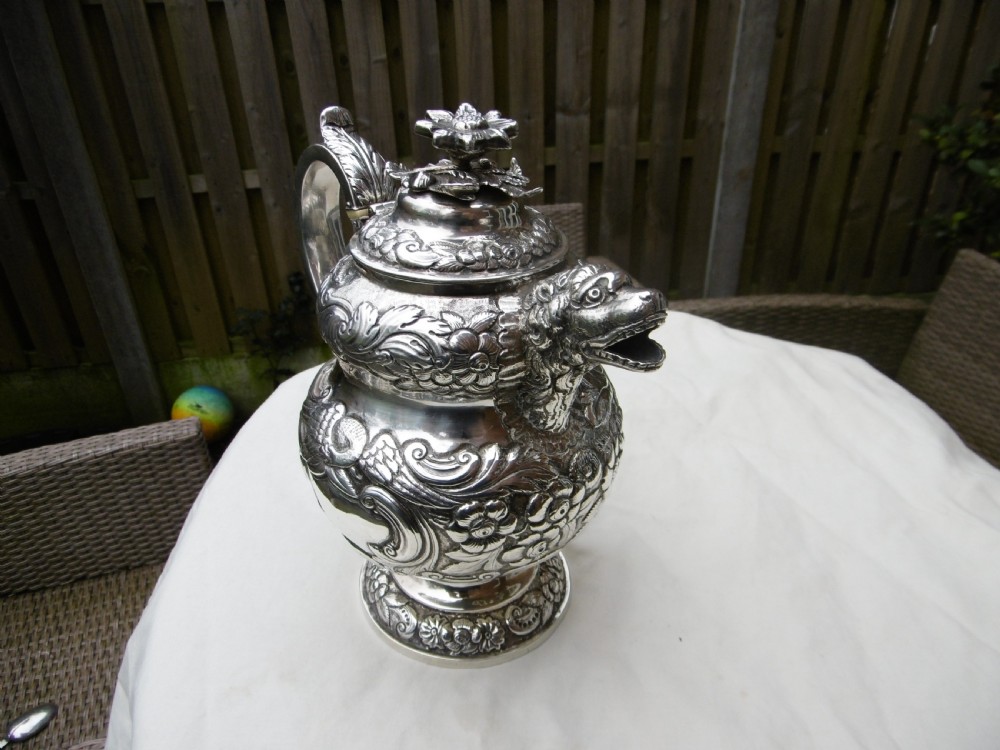 An ornate Georgian sterling silver coffee pot featuring intricate floral repousse chasing, a flower finial, and a cast animal head spout.
