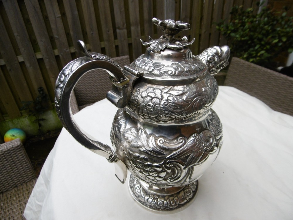 An ornate Georgian sterling silver coffee pot featuring intricate floral repousse chasing, a flower finial, and a cast animal head spout. View II