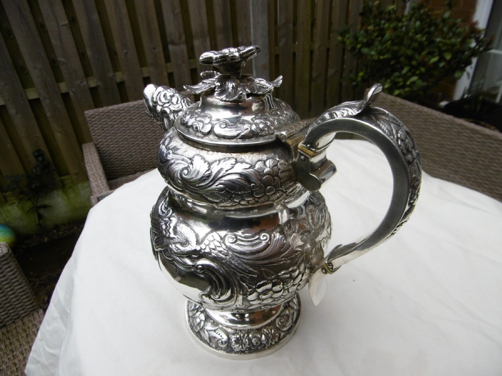 An ornate Georgian sterling silver coffee pot featuring intricate floral repousse chasing, a flower finial, and a cast animal head spout. View III