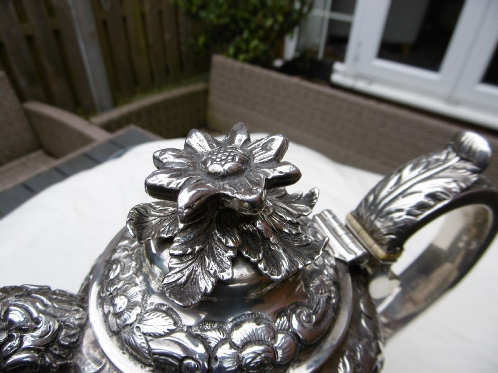 An ornate Georgian sterling silver coffee pot featuring intricate floral repousse chasing, a flower finial, and a cast animal head spout. View IV