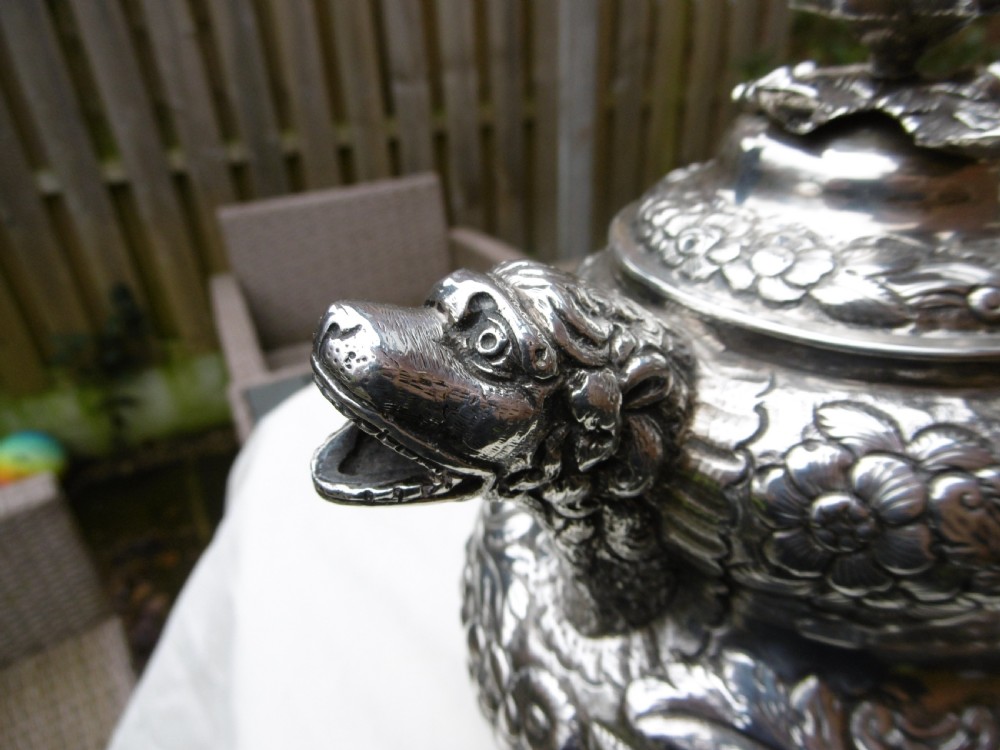 An ornate Georgian sterling silver coffee pot featuring intricate floral repousse chasing, a flower finial, and a cast animal head spout. View V
