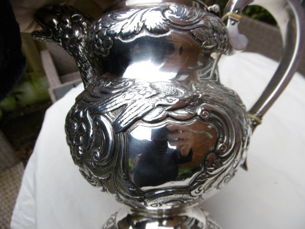 An ornate Georgian sterling silver coffee pot featuring intricate floral repousse chasing, a flower finial, and a cast animal head spout. View VI