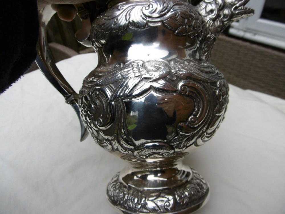An ornate Georgian sterling silver coffee pot featuring intricate floral repousse chasing, a flower finial, and a cast animal head spout. View VII