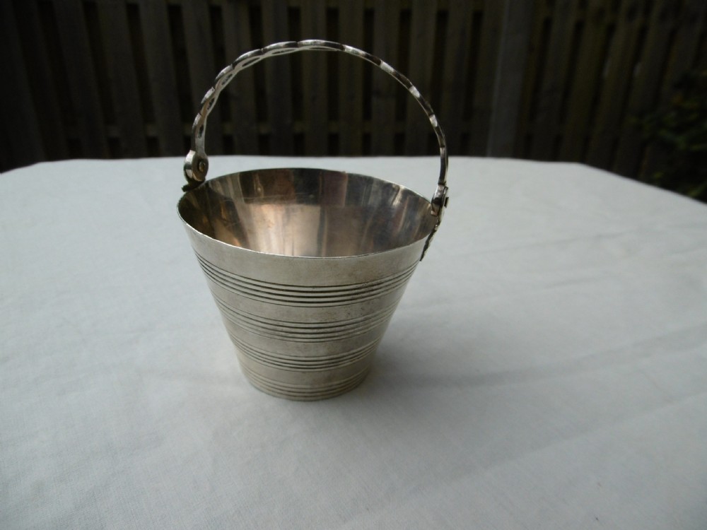 A Georgian sterling silver cream pail featuring a tapered bucket shape decorated with horizontal reeded lines and an overhead swing handle.