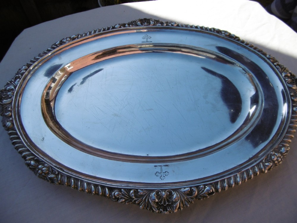 An oval Georgian sterling silver platter featuring a cast shell and gadrooned border with an engraved heraldic crest.