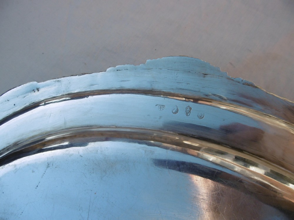 An oval Georgian sterling silver platter featuring a cast shell and gadrooned border with an engraved heraldic crest. View II