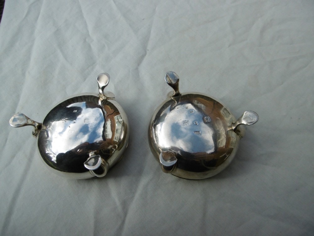 A pair of circular Scottish Georgian sterling silver open salt cellars with hoof feet alongside matching small silver salt spoons. View II