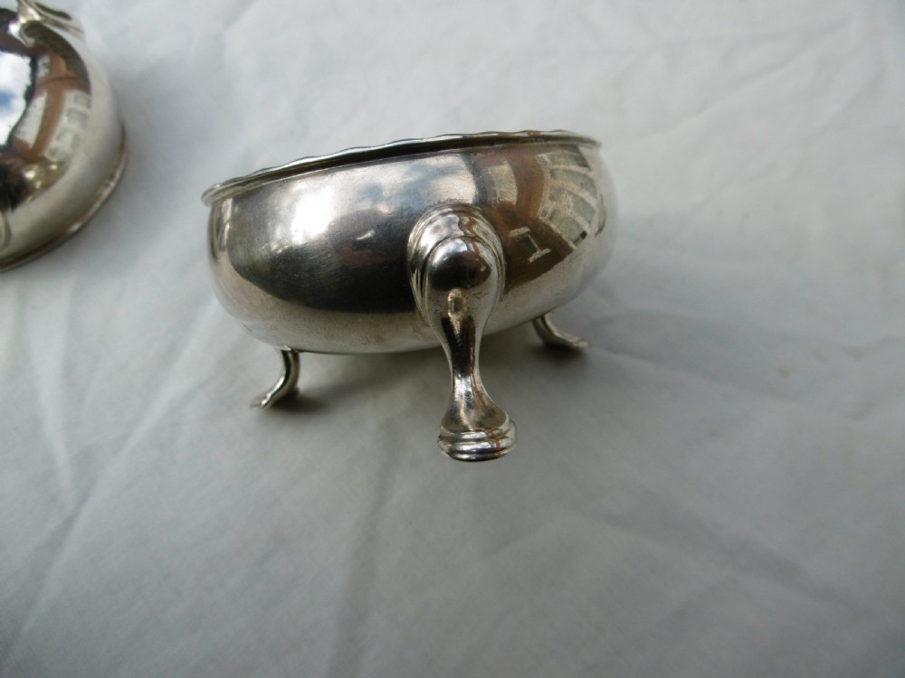 A pair of circular Scottish Georgian sterling silver open salt cellars with hoof feet alongside matching small silver salt spoons. View V