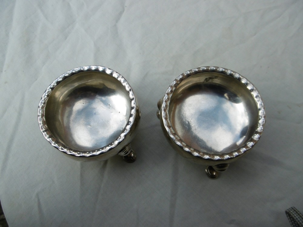A pair of circular Scottish Georgian sterling silver open salt cellars with hoof feet alongside matching small silver salt spoons. View VI