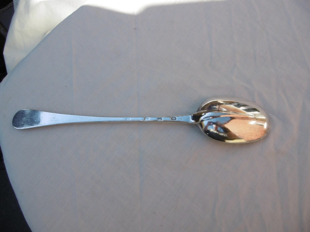 A George I Britannia standard silver basting spoon featuring a long tapered handle and an oval bowl with a rat-tail joint.