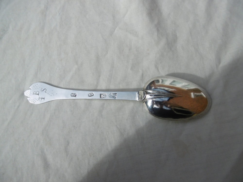 An antique silver William III trefid spoon with stamped hallmarks along the flat stem, engraved initials on the notched terminal, and a rat-tail bowl attachment.