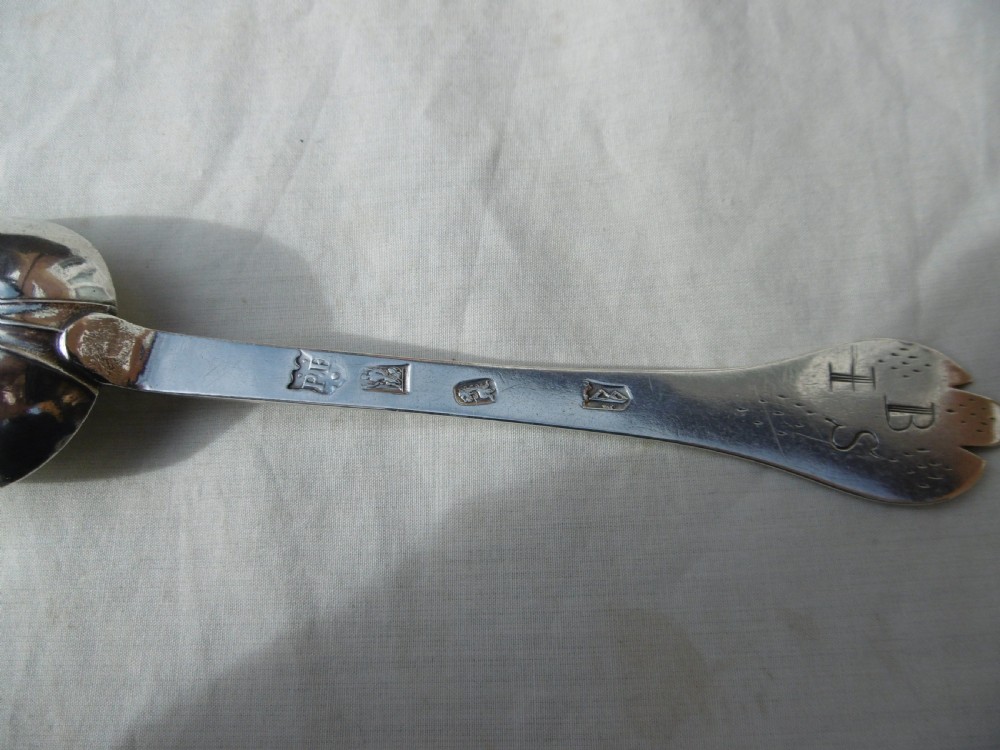 An antique silver William III trefid spoon with stamped hallmarks along the flat stem, engraved initials on the notched terminal, and a rat-tail bowl attachment. View III