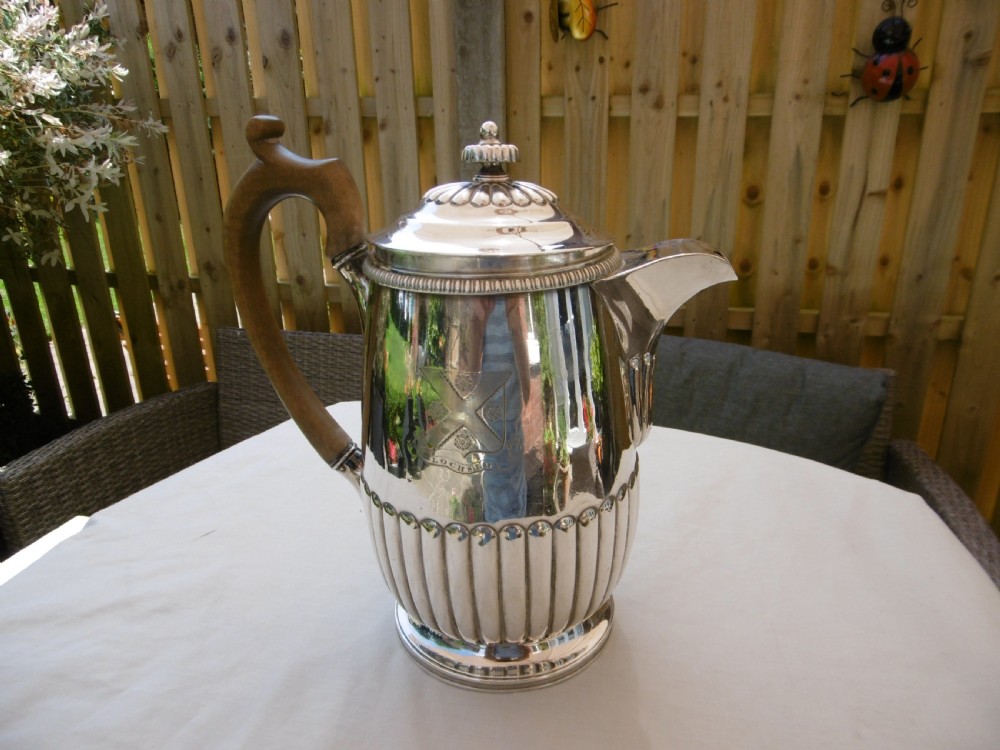 A Georgian silver coffee pot featuring fluted lower body detailing, an engraved crest, and a carved wooden handle.