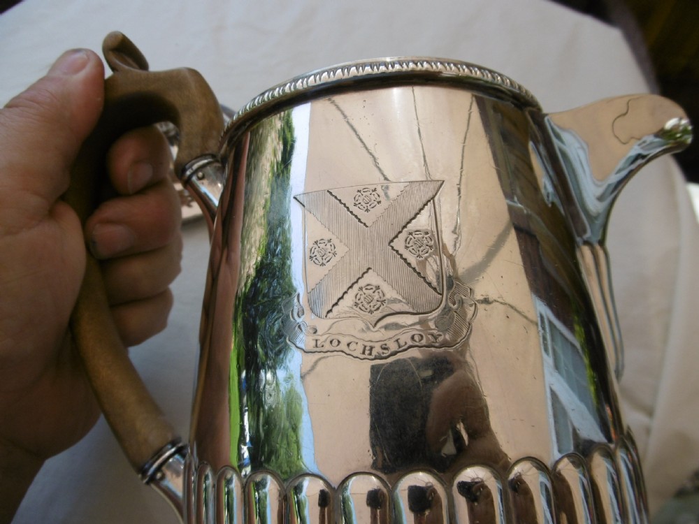 A Georgian silver coffee pot featuring fluted lower body detailing, an engraved crest, and a carved wooden handle. View V
