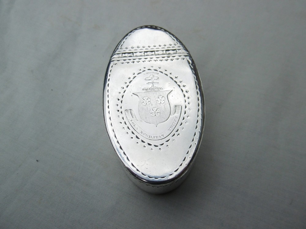 An oval Georgian silver snuff box decorated with bright-cut engraving and an armorial coat of arms.