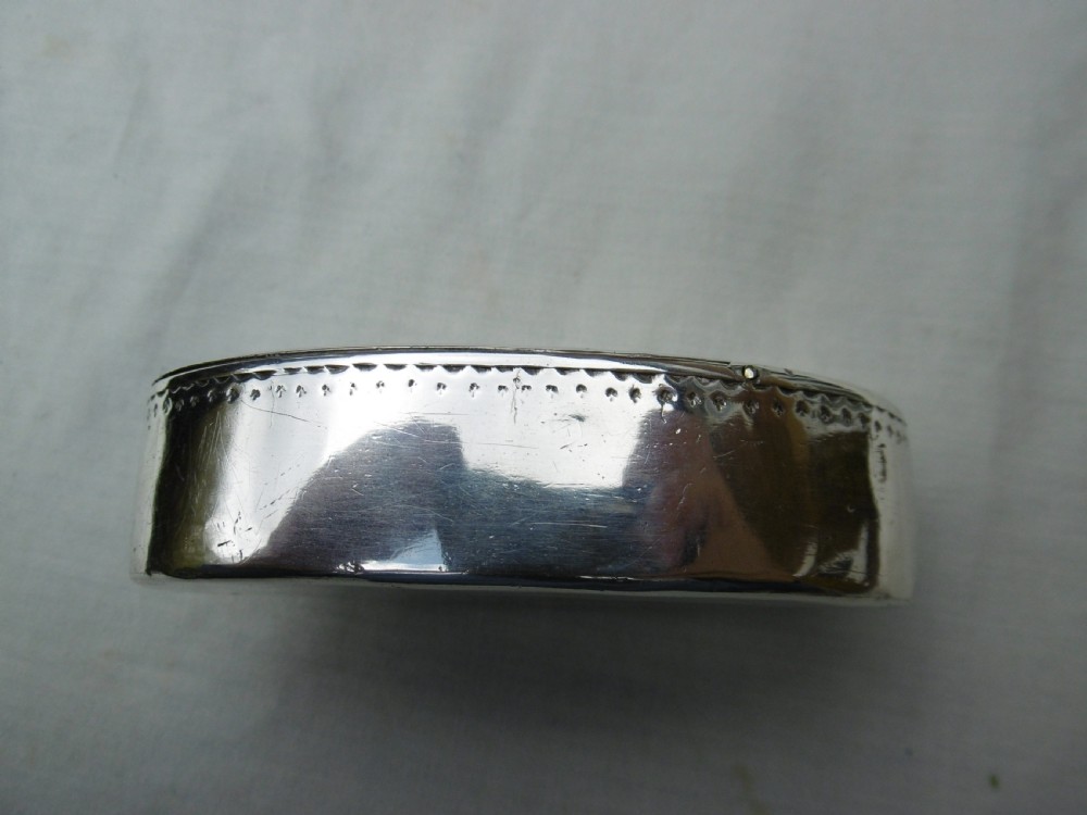 An oval Georgian silver snuff box decorated with bright-cut engraving and an armorial coat of arms. View V
