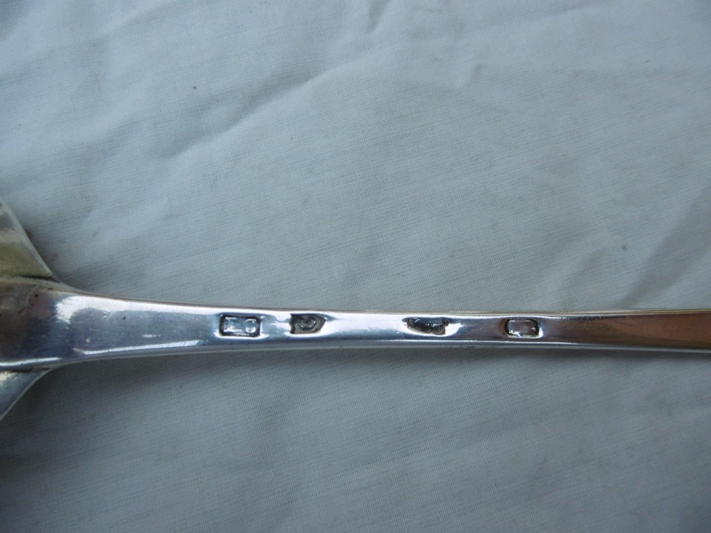 An 18th-century Irish Georgian sterling silver basting spoon featuring a tapered stem with an engraved family crest and a distinctive hooked handle terminal. View II
