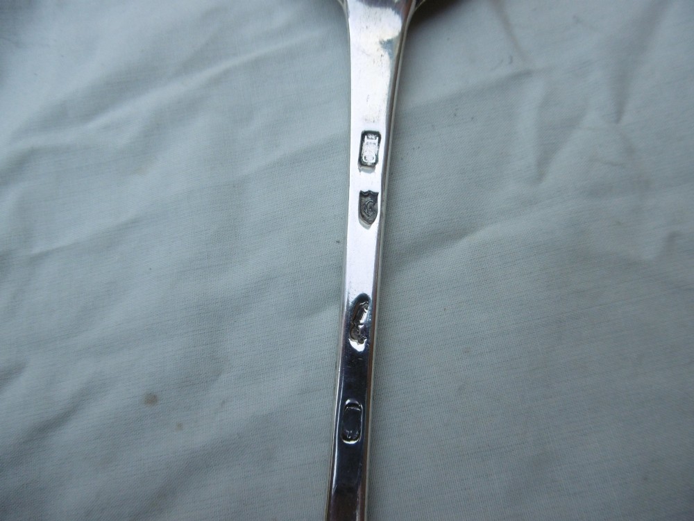 An 18th-century Irish Georgian sterling silver basting spoon featuring a tapered stem with an engraved family crest and a distinctive hooked handle terminal. View III